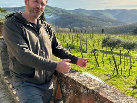 Diego Finocchi standing by stone railing with Erta di Radda vineyard and hills in background