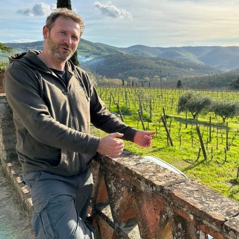 Diego Finocchi standing by stone railing with Erta di Radda vineyard and hills in background