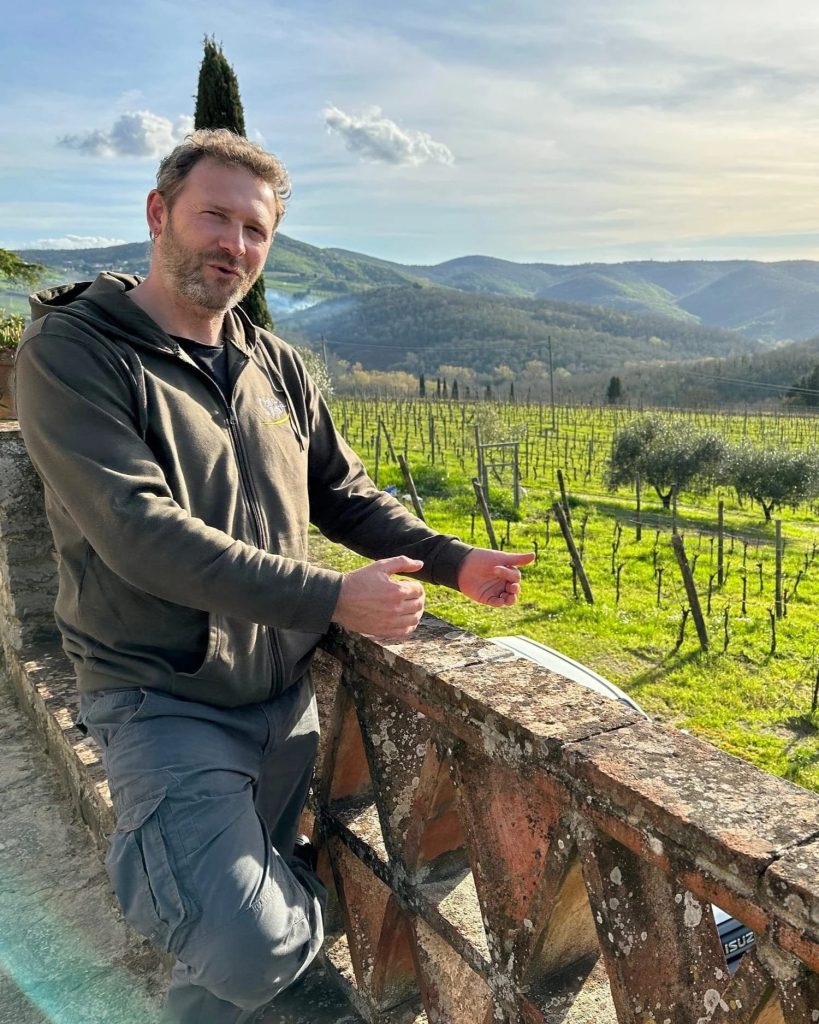 Diego Finocchi standing by stone railing with Erta di Radda vineyard and hills in background