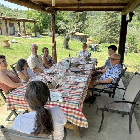 Guests seated at a long outdoor table under a wooden shelter at Podere Somigli farm