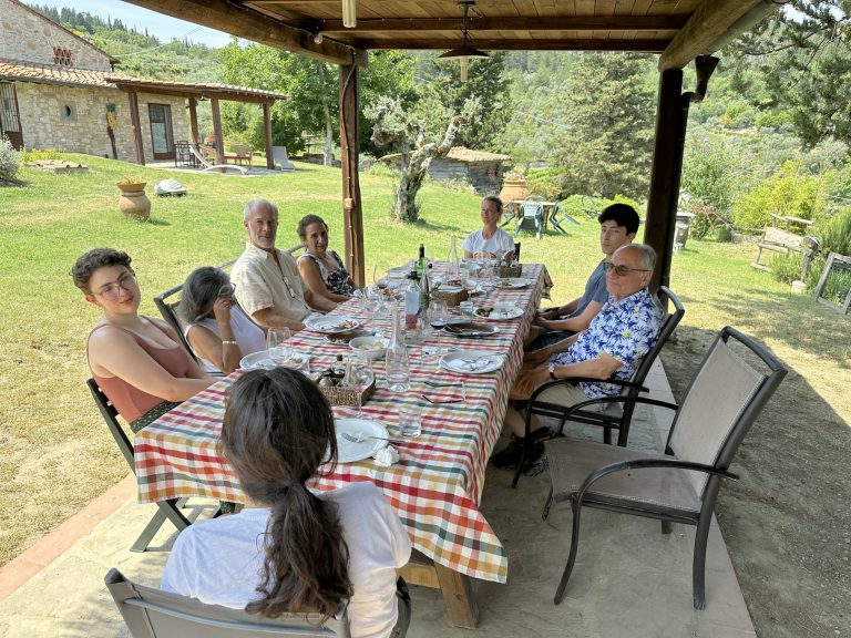 Guests seated at a long outdoor table under a wooden shelter at Podere Somigli farm