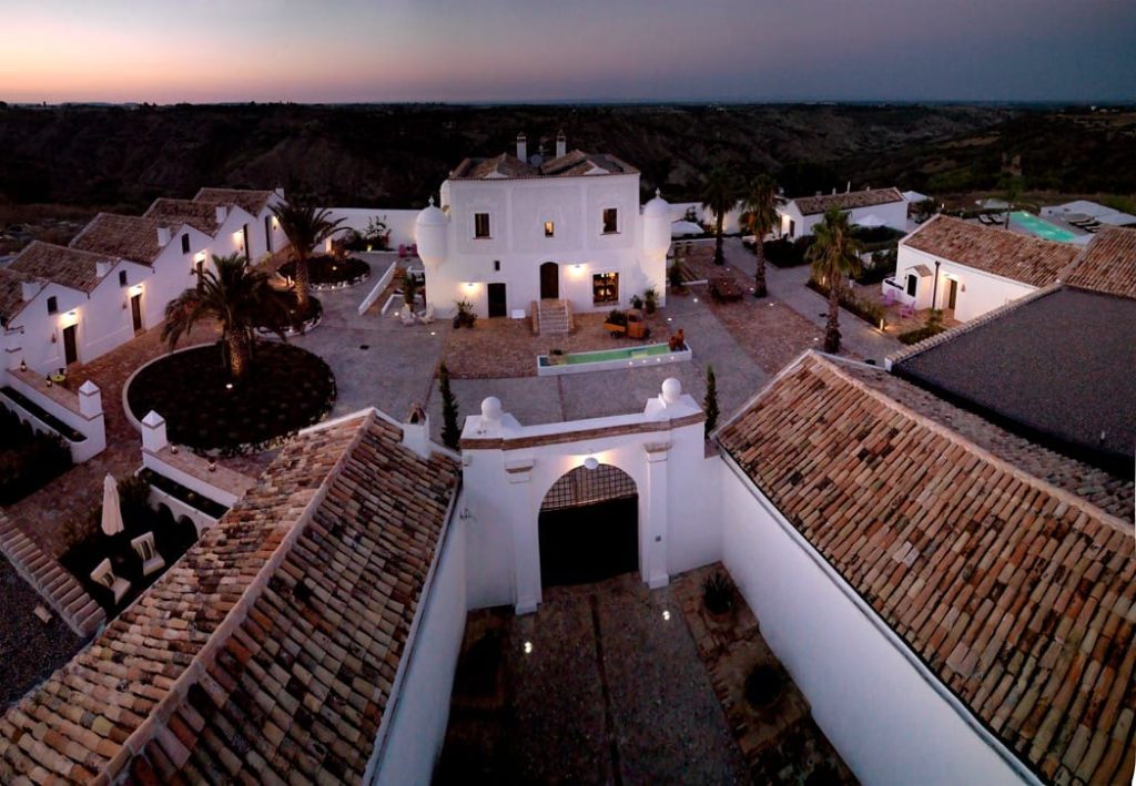 Aerial view of Torre Fiore boutique hotel at dusk, white buildings around a courtyard in Pisticci