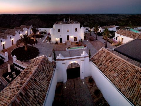 Aerial view of Torre Fiore boutique hotel at dusk, white buildings around a courtyard in Pisticci
