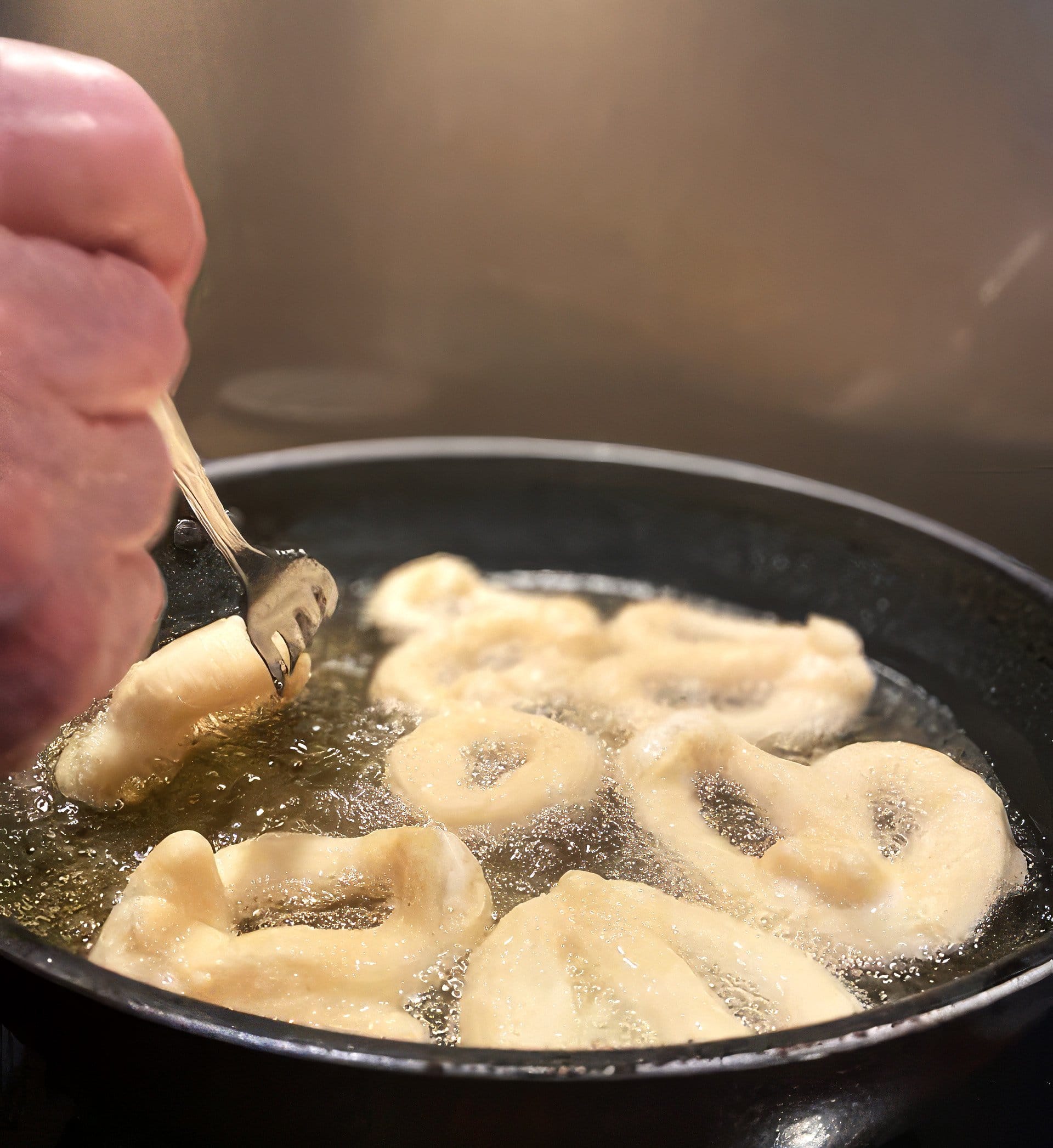 Close-up of zeppoli frying in oil in a pan with a hand holding a fork placing a piece.