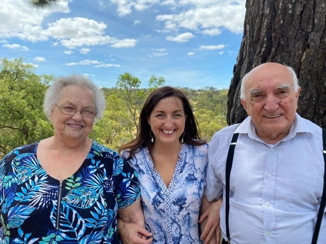 Mum, Franca, and Dad, standing outdoors with trees and blue sky behind them.
